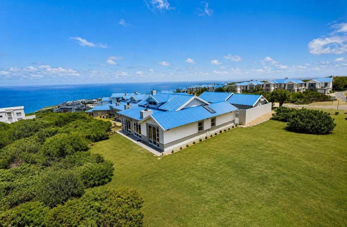 ONPOINT27 Pinnacle Point Lodge exterior: white holiday home with blue roofs, garden lawn and Indian Ocean backdrop