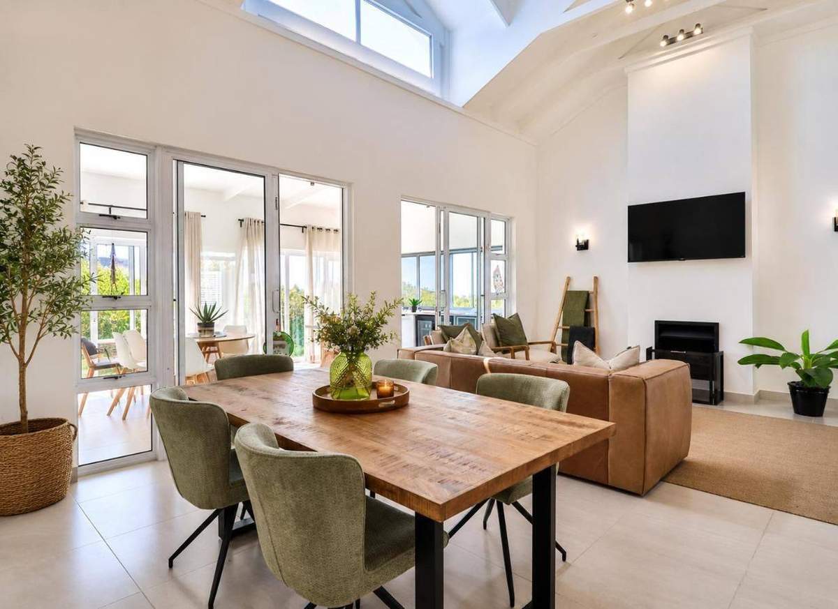 Open-plan living and dining room with sage chairs, leather sofa and sea-facing glass doors at ONPOINT27, Pinnacle Point
